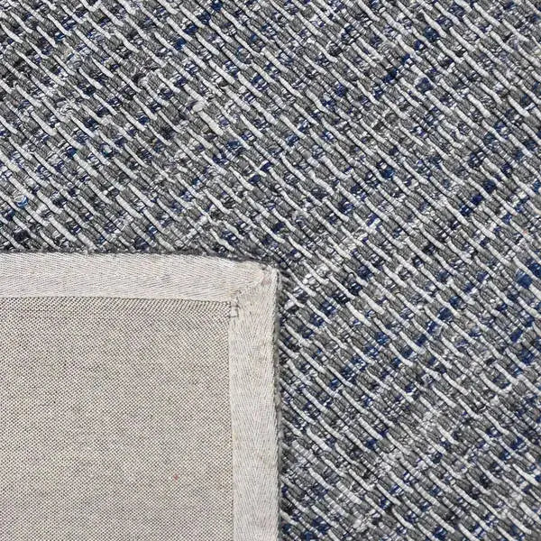 Achterkant hoek aanzicht van het vloerkleed HUXLEY in de kleur Denim Blauw, gemaakt van Wol en Viscose mix.