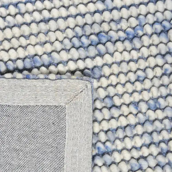 Achterkant hoek aanzicht van het vloerkleed MIRANDE in de kleuren Licht Blauw / Beige, gemaakt van 100% Wol.